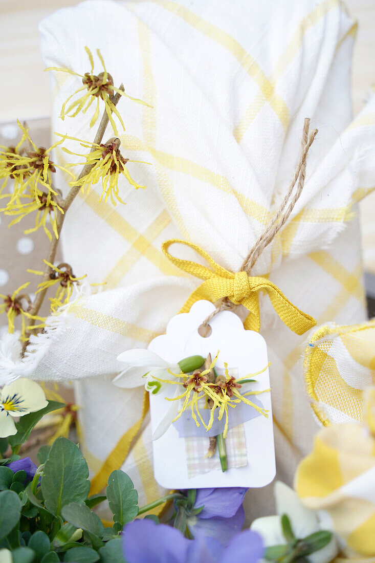 Geschenk mit Frühlingsblumen in gelb-weißem Tuch und Anhänger