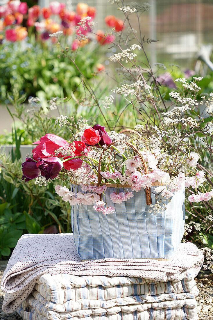 Tasche mit Frühlingsblumen auf einer Decke und Kissen im Garten