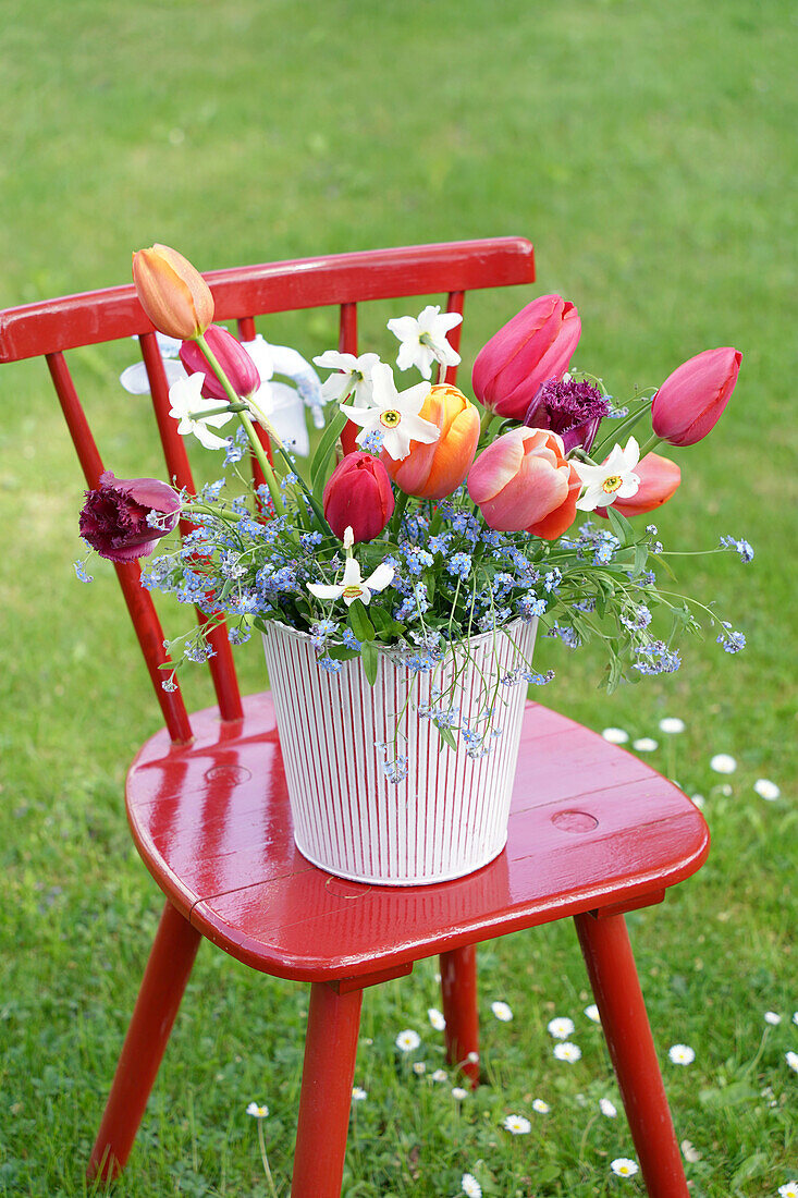Frühlingsblumenarrangement auf rotem Stuhl im Garten
