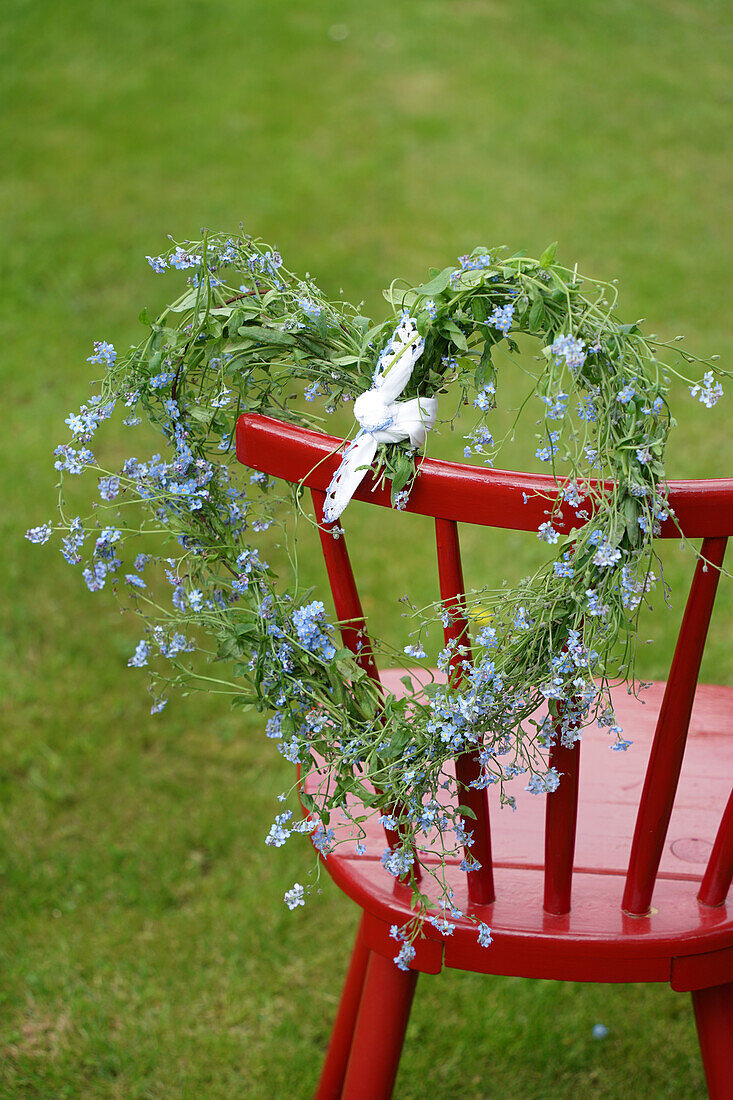 Roter Stuhl mit blau blühendem Kranz in Herzform im Garten