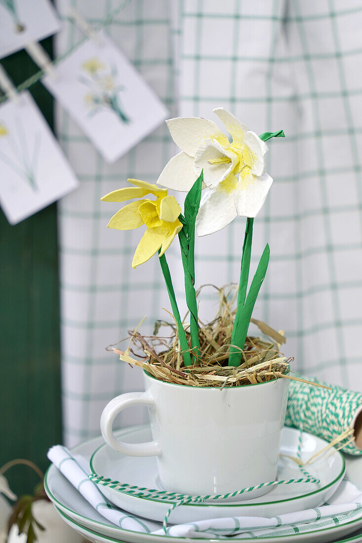 Crafted daffodils in a white cup decorated with straw
