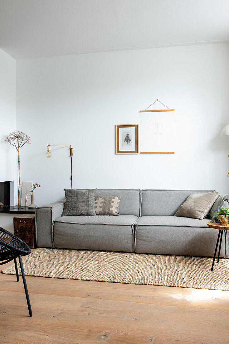 Minimalistisches Wohnzimmer mit grauem Sofa, Juteteppich und Wanddekoration