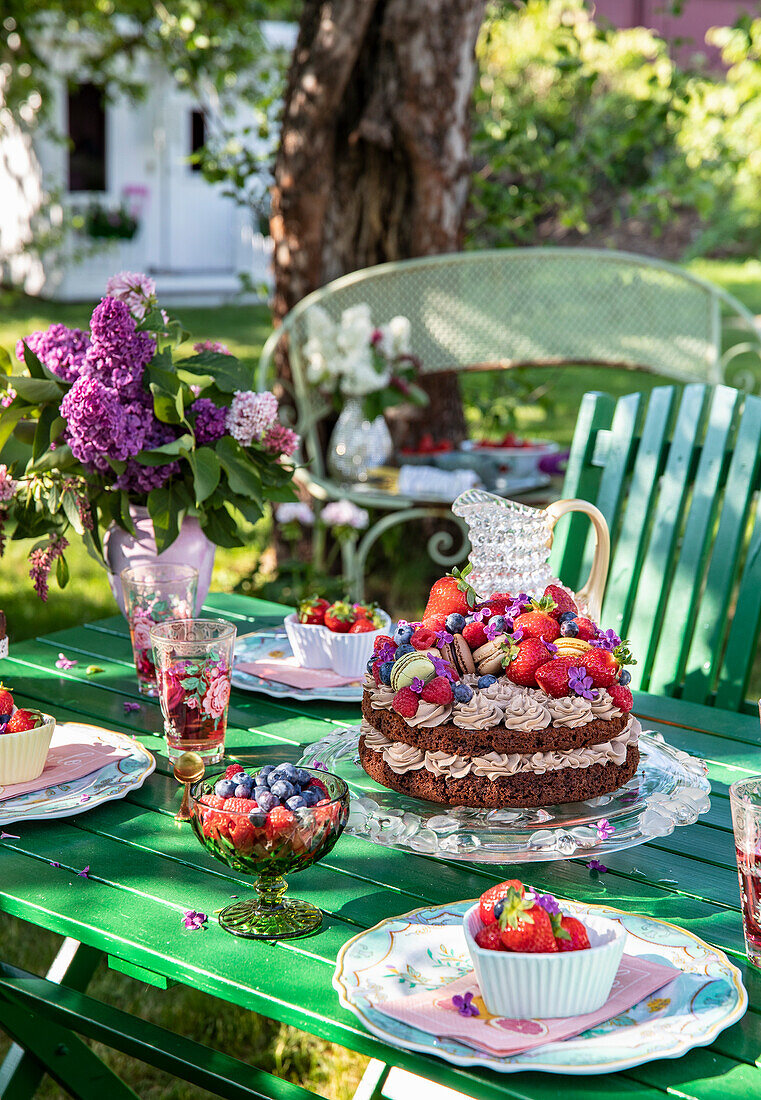 Gartentisch mit Schokoladentorte und Sommerblumen in einer Vase