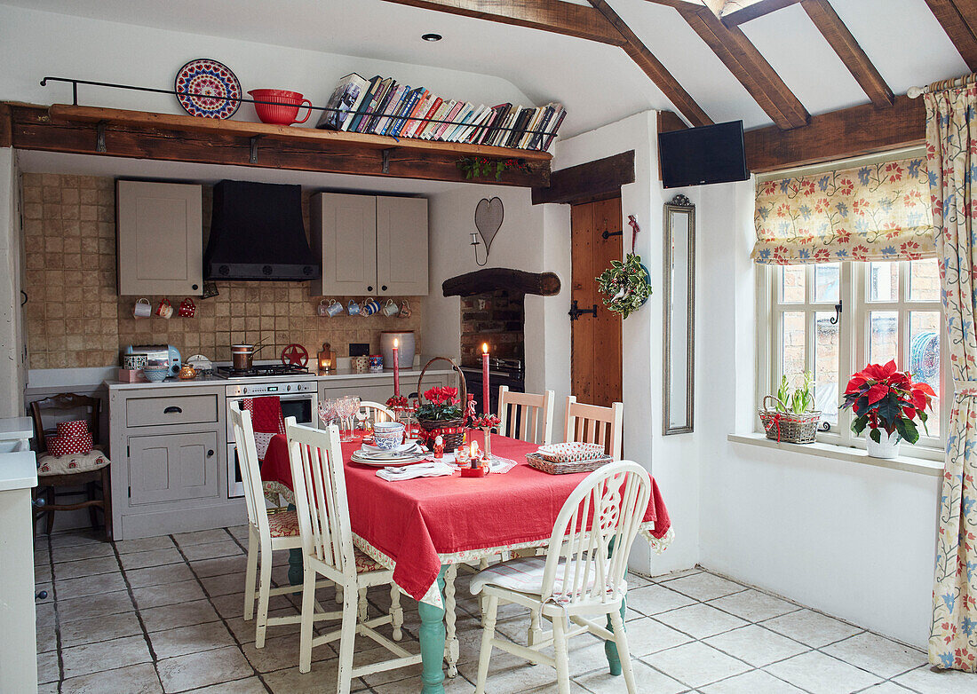 High book shelf with red tablecloth on dining table in, UK farmhouse kitchen