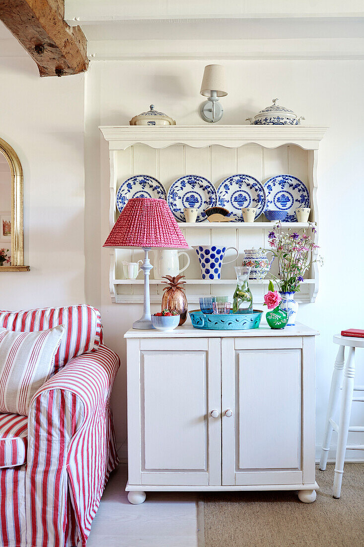 Dekorative Teller auf einem Regal über einem Schrank mit einer Gingham-Lampe in einem britischen Landhaus