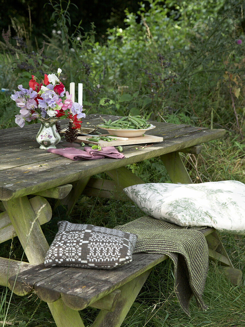 Garden table with tableware and flower and bench with rug