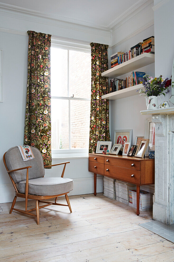 Grauer Sessel und Retro-Sideboard mit Bücherregalen am Fenster eines Familienhauses in Colchester, Essex, England, UK