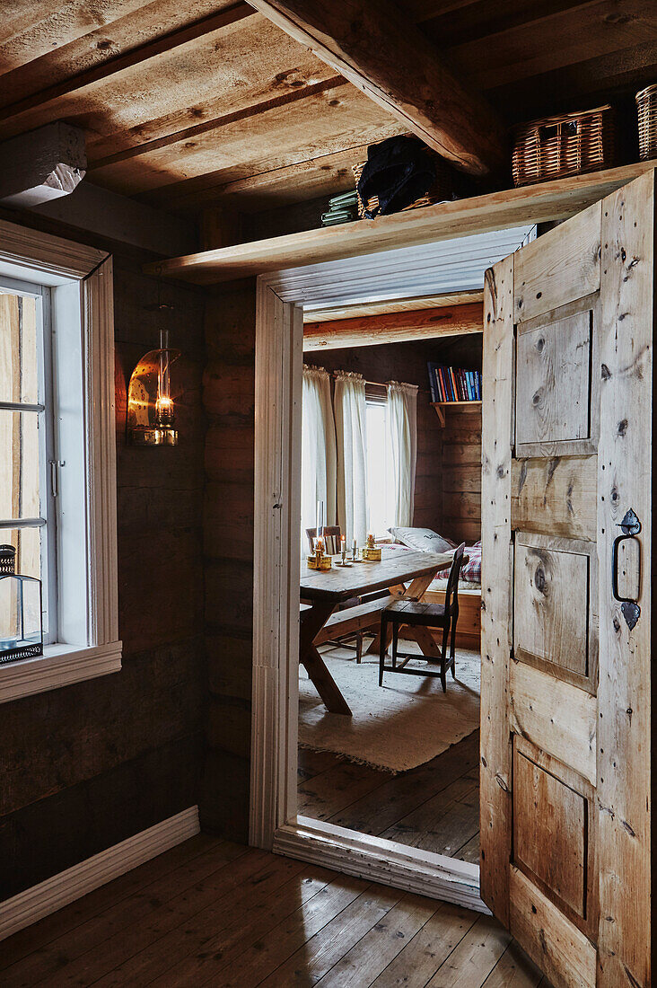Blick aus der holzverkleideten Diele durch offene Tür ins Kinderzimmer mit Tisch, in einer Holzhütte in den Bergen von Sirdal, Norwegen