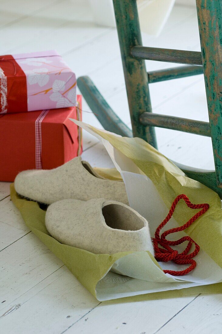 Hausschuhe mit Geschenkpapier auf weißem Holzboden und zwei eingepackte Weihnachtsgeschenke
