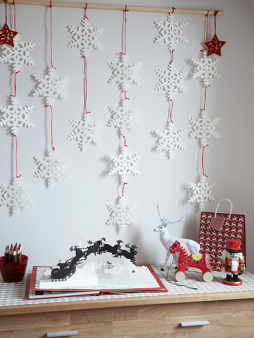 Snowflake wall decoration and pop-up Christmas book on chest of drawers in family home, Poland