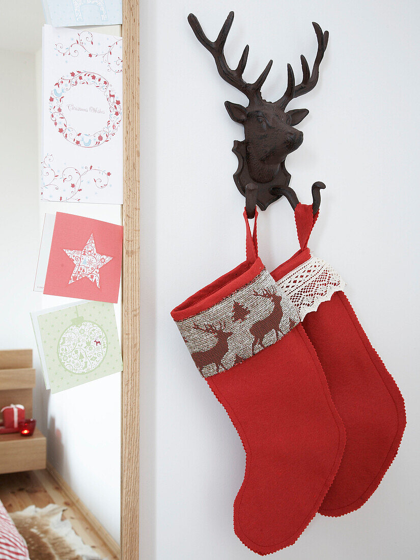 Christmas stockings hang on reindeer hook next to mirror with greetings cards in Polish family home
