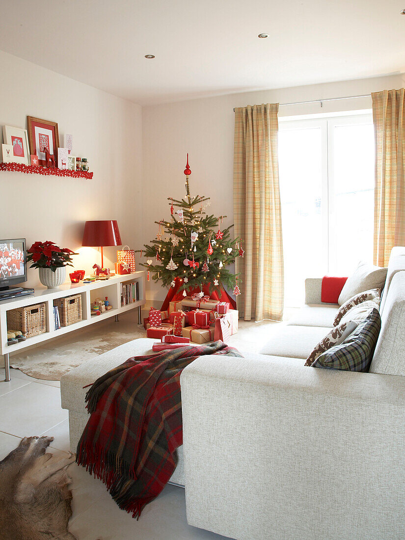 Tartan-Decke auf Ottomane mit weißem Sofa in einem weihnachtlichen polnischen Familienhaus