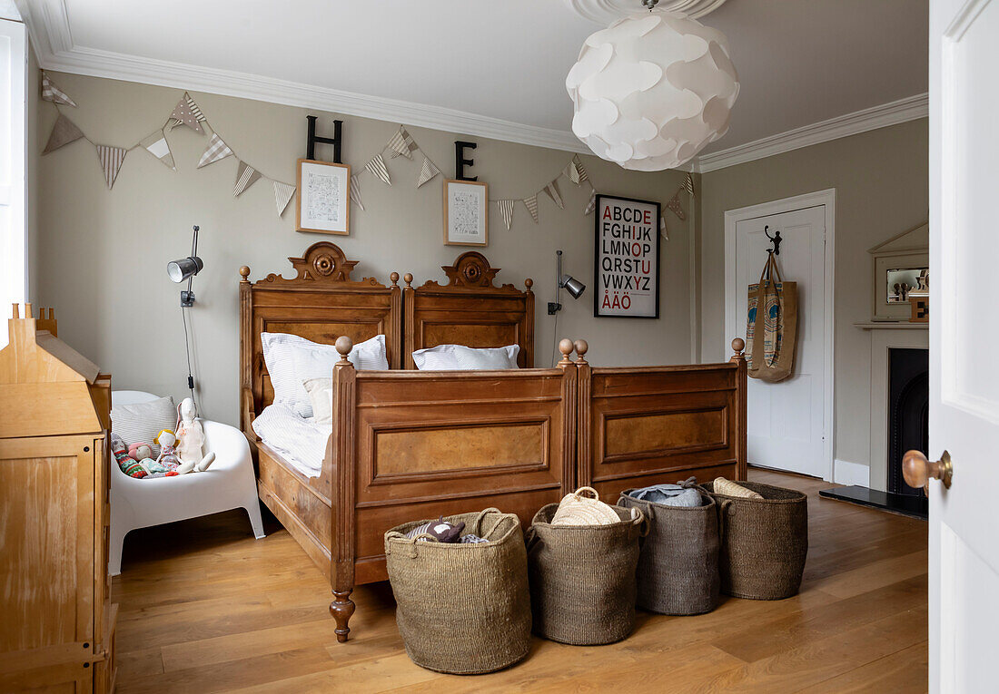 Two antique single beds fixed together with storage baskets in girls room of Woodbridge home Suffolk UK