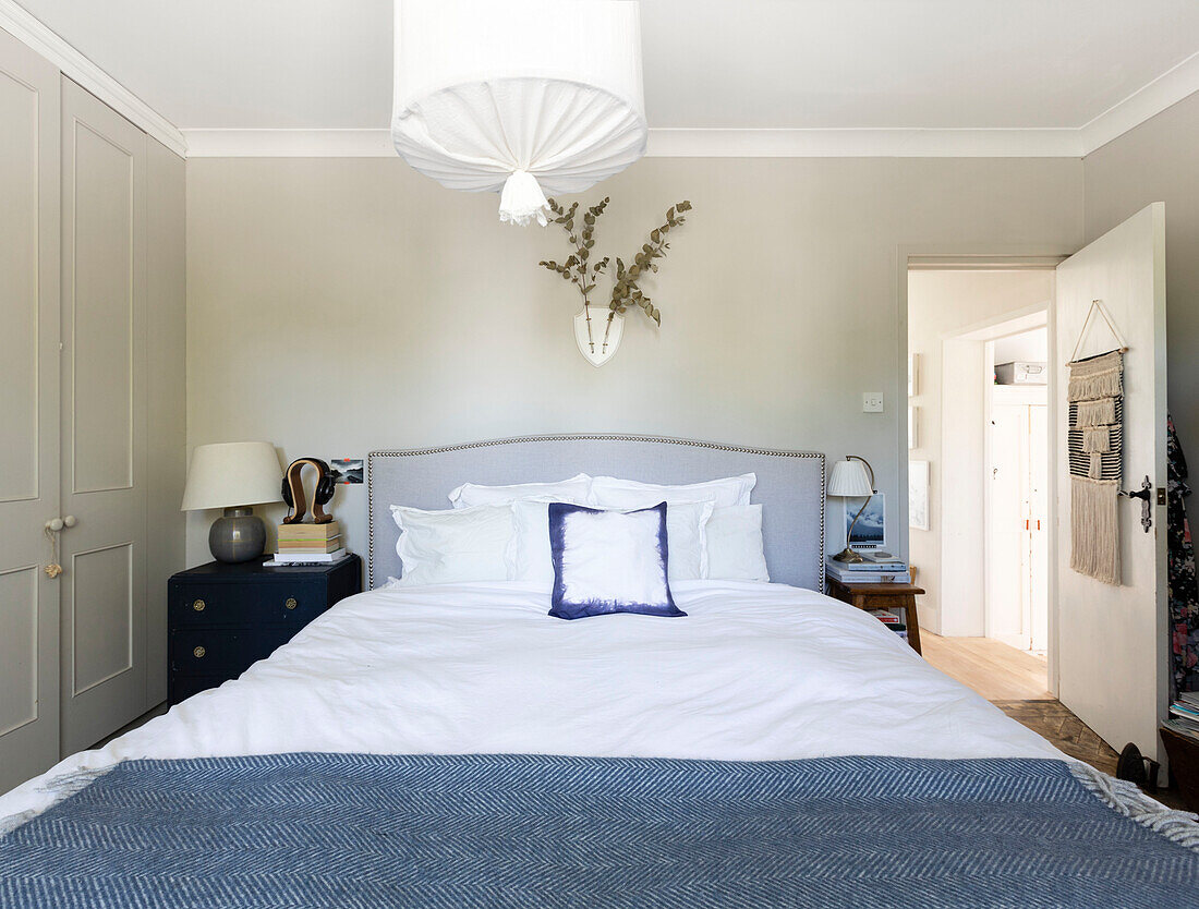 Eukalyptus über dem Bett mit upgecycelten Nachttischen und einer aus Holzreifen und Musselin gefertigten Leuchte in einem Haus in Colchester, Essex, Großbritannien