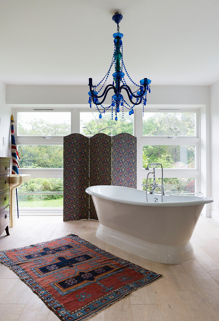 Freistehende Badewanne und gemusterter Teppich mit Faltwand am Fenster in einem Haus in Guildford, Surrey, UK
