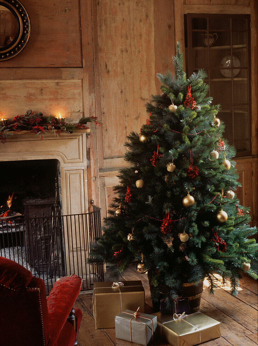 Geschmückter Weihnachtsbaum in einem holzgetäfelten Wohnzimmer mit offenem Kamin