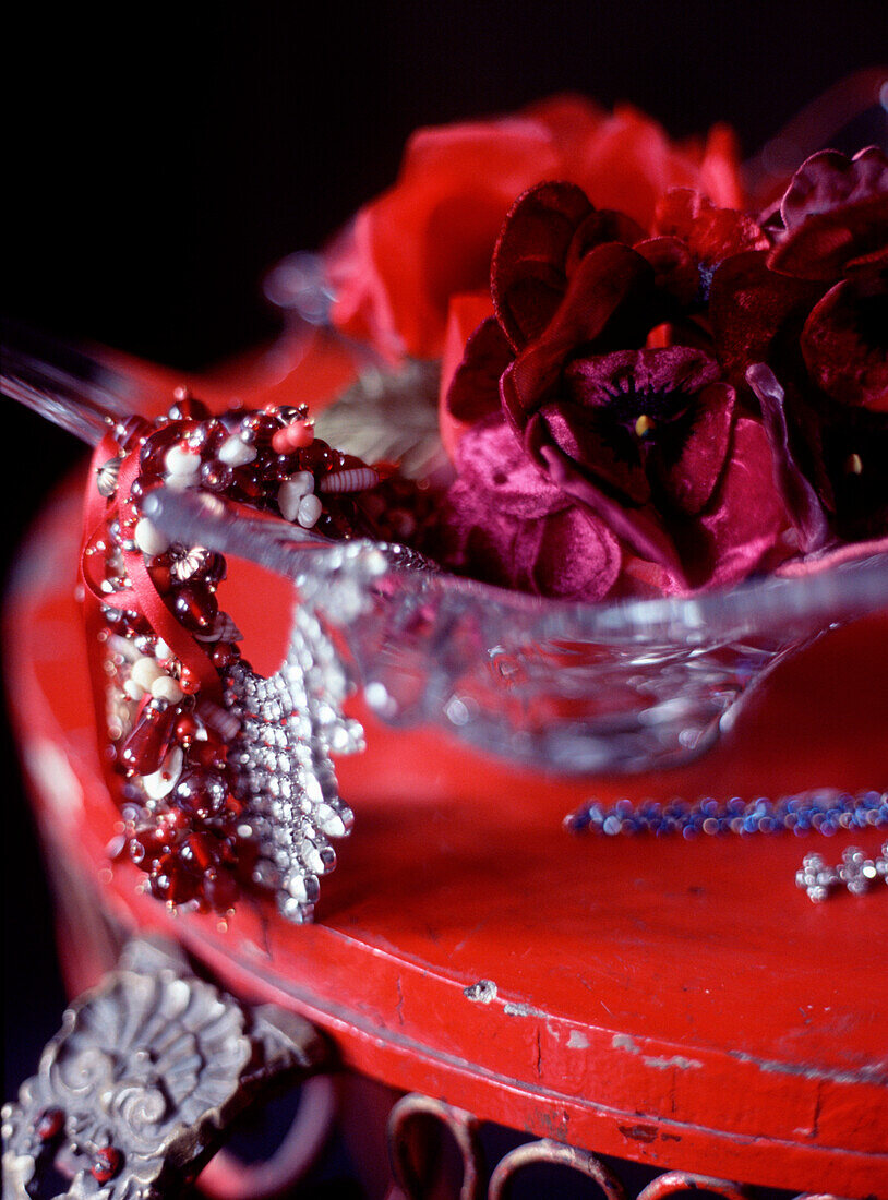 Eine Glasschale auf einem rustikalen Schminktisch mit Seidenblumen und Schmuck