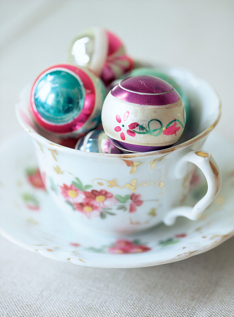 A floral vintage style cup and saucer displaying a collection of Christmas baubles