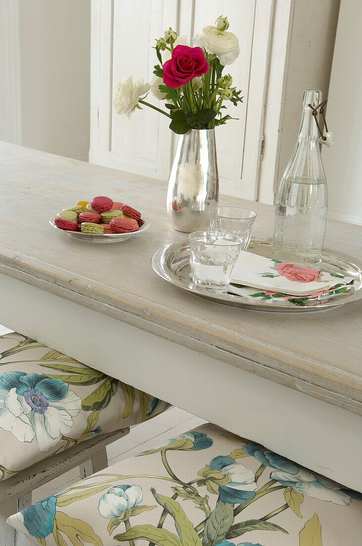 Vase mit frischen Blumen Tablett mit Getränken und Keksen auf einem weißen Esstisch
