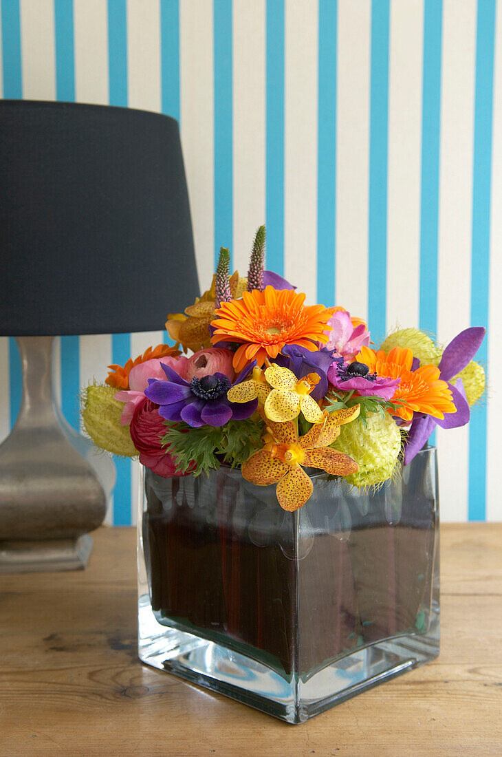 Colourful fresh cut flower display on tabletop with lamp and stripy wallpaper