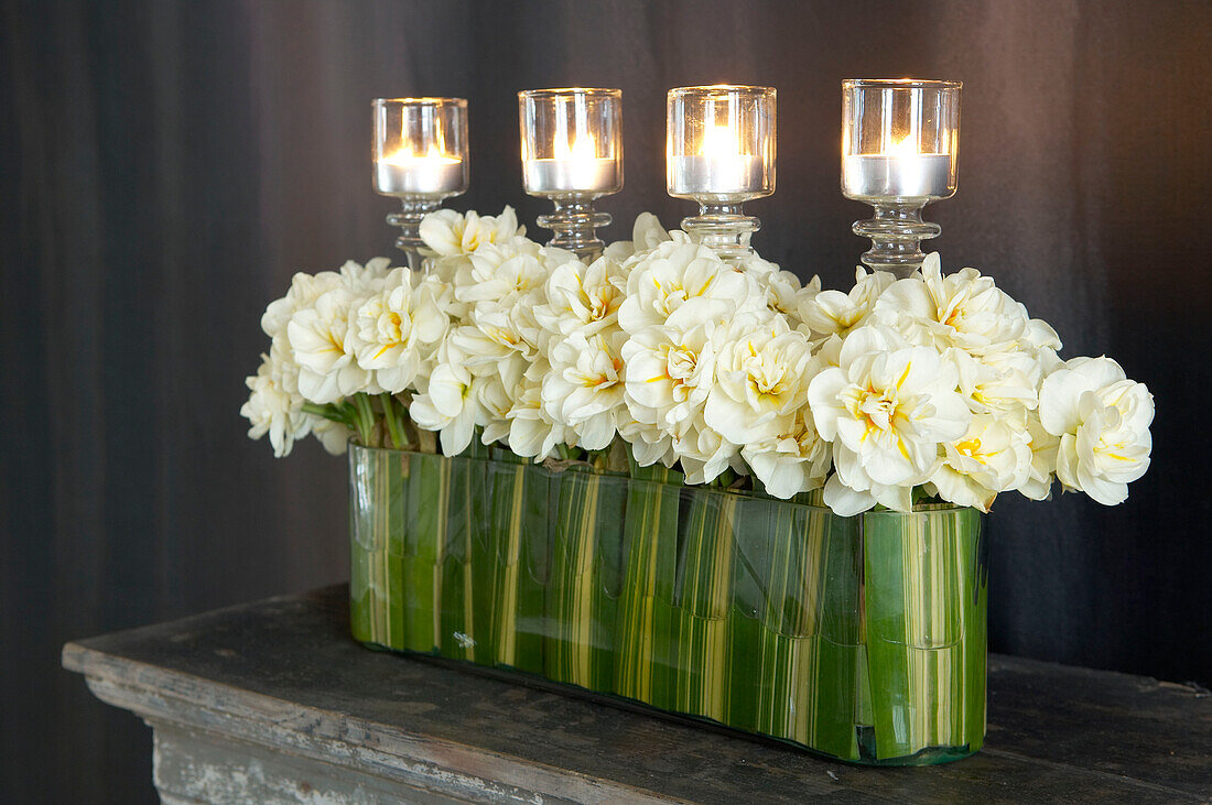 Zeitgenössisches Blumenarrangement aus frischen weißen Blumen auf einem Kaminsims mit brennenden Kerzen in Kerzenhaltern