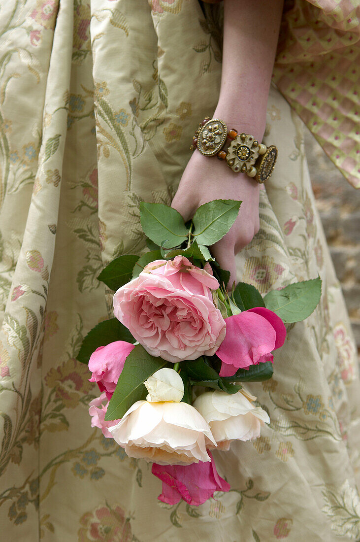 Frau hält einen Strauß frisch geschnittener rosa und weißer Rosen in einem Blumenkleid