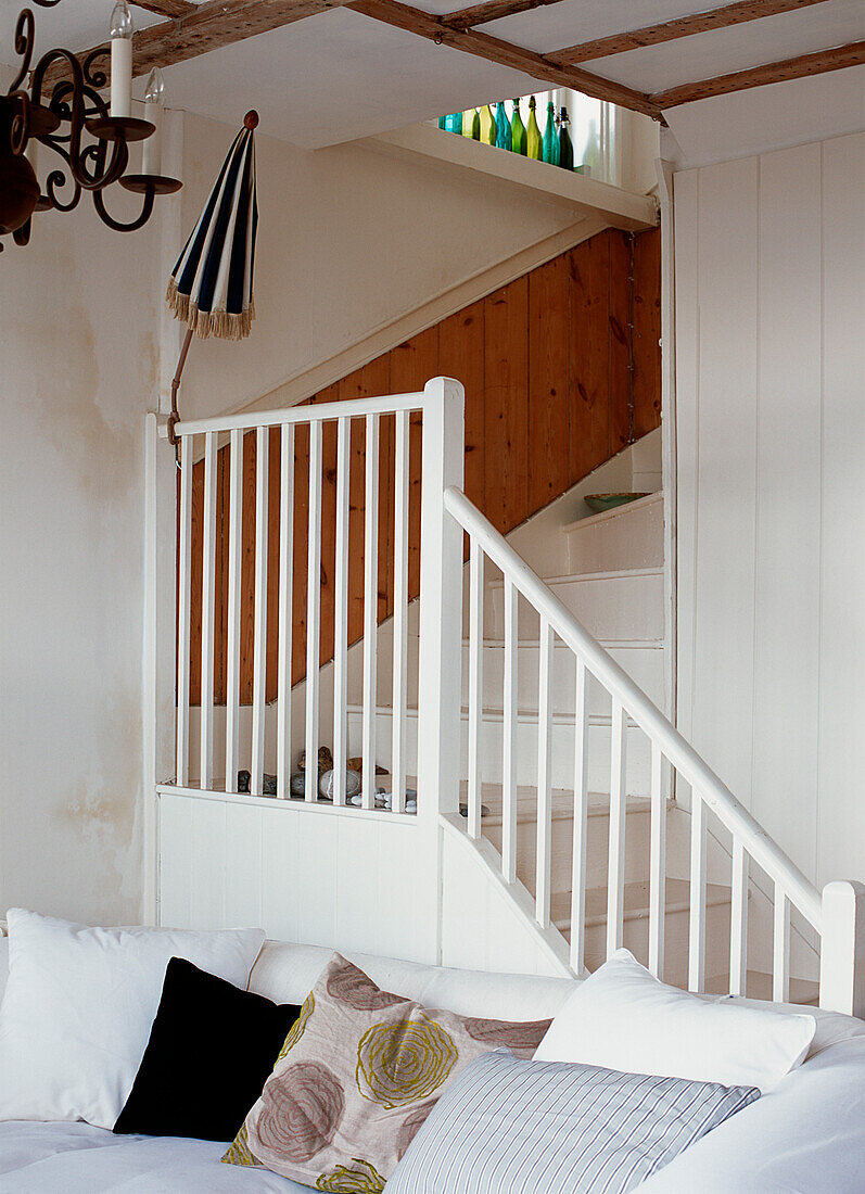 Blick vom Wohnzimmer auf eine weiß gestrichene Treppe mit Nut- und Federverkleidung