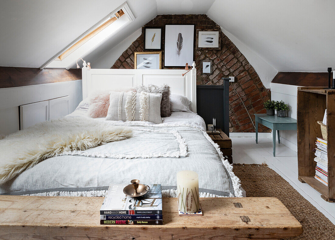 Attic bedrooom with double bed and exposed brick wall displaying feather artwork multi-textured with fabrics and skins and wooden furniture Cardiff Wales UK