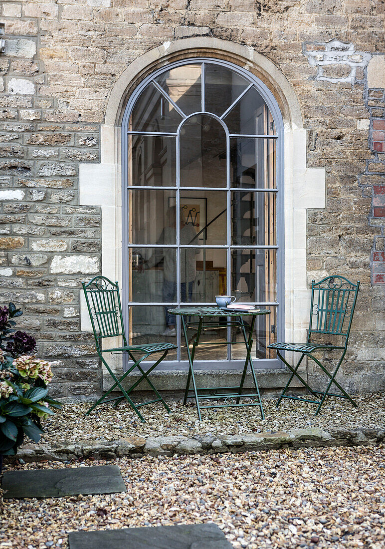 Tisch und Stühle vor dem gewölbten georgianischen Fenster des Hauses der Schmuckdesignerin Ellie Swinhoe in Somerset, UK