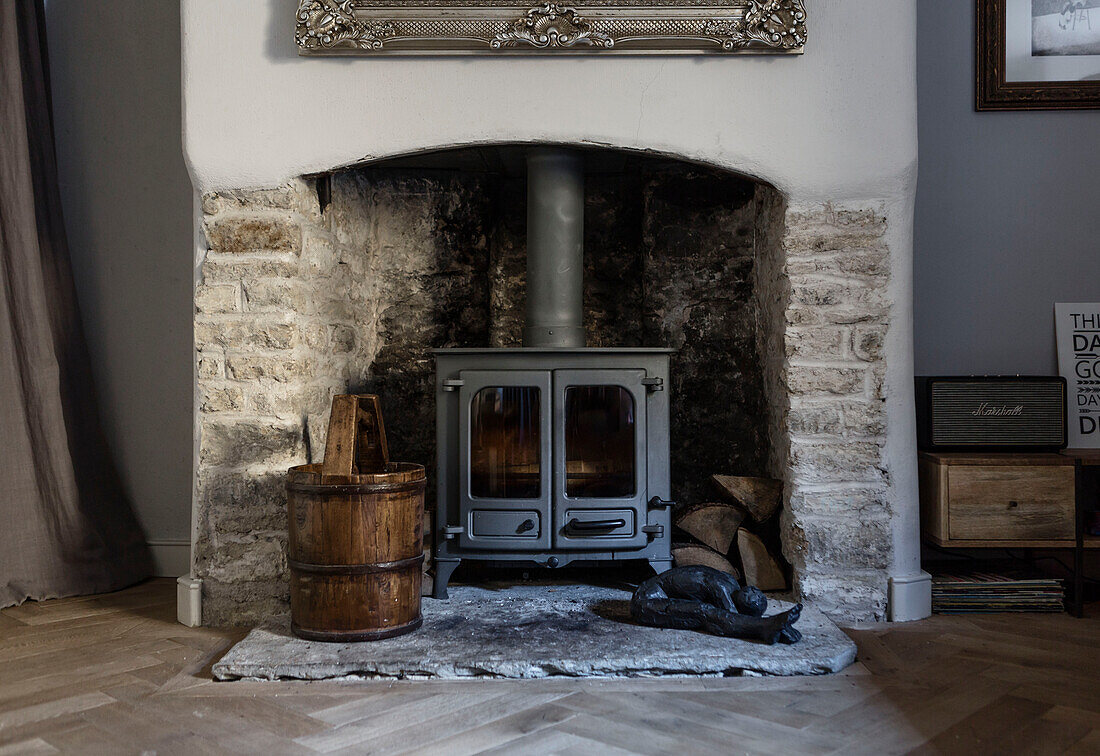 Holzofen mit antikem Eimer in offenem Steinkamin in einem Hause in Somerset, UK