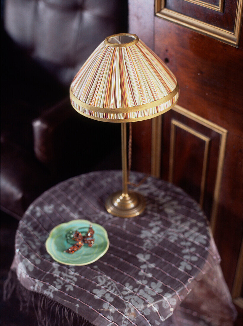 Beistelltisch mit Lampe und gemustertem Tischtuch im Wohnzimmer