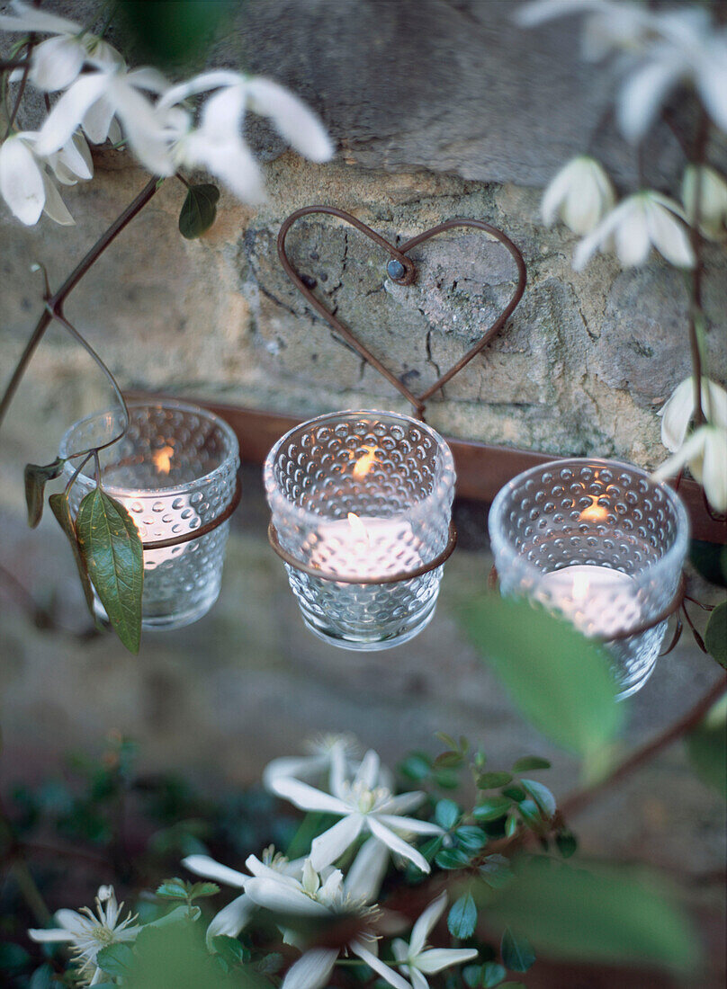 Herzförmiger Metallbügel mit brennenden Teelichtern inmitten von weißen Frühlingsblumen