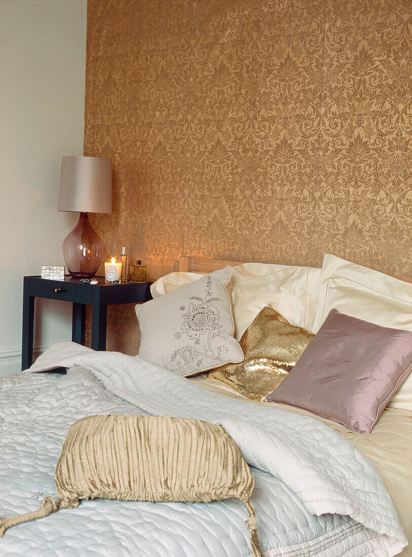 A tableaux of silk and satin cushions on a double bed against decorative gold wall covering 