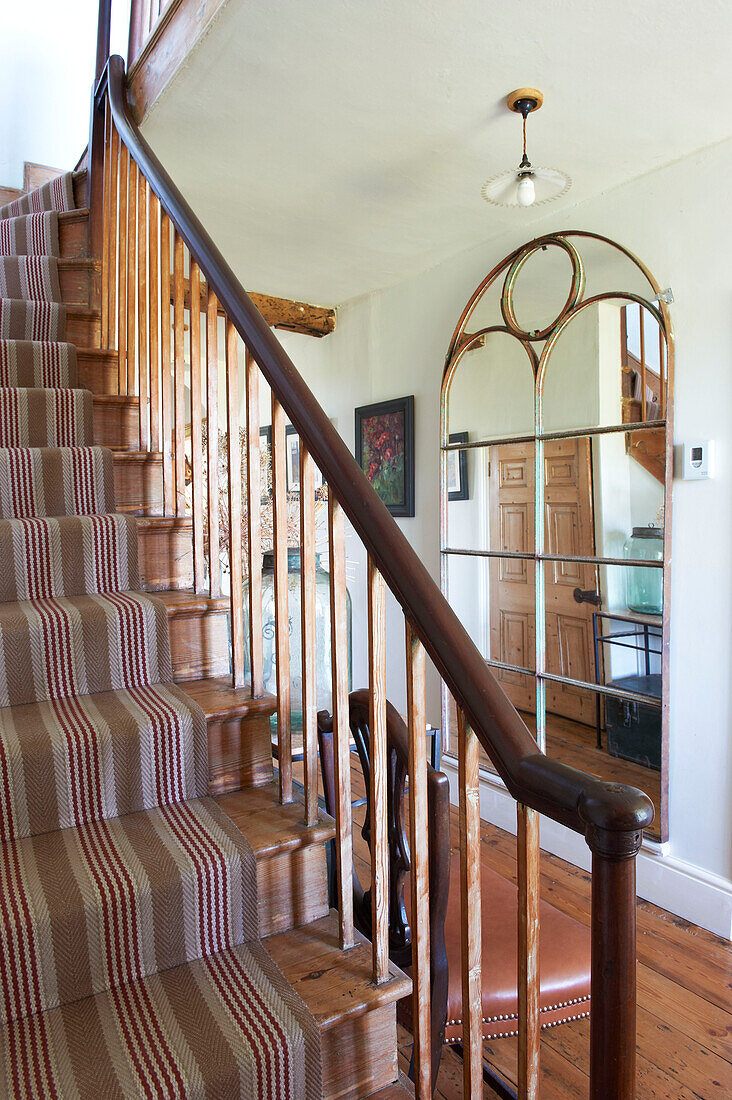 Carpeted staircase and antique mirror in hallway of Iden farmhouse, Rye, East Sussex, UK