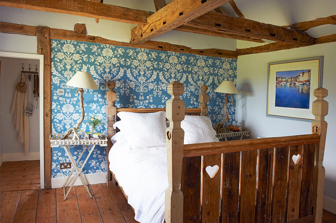 In das hölzerne Fußteil des Bettes geschnitzte Herzen in einem blau tapezierten Zimmer im Fachwerkbauernhaus Iden, Rye, East Sussex, Vereinigtes Königreich