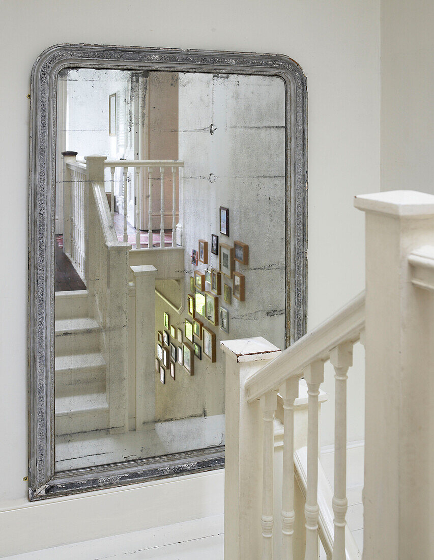 Framed pictures reflected in old mirror on staircase landing in Hereford home, England, UK