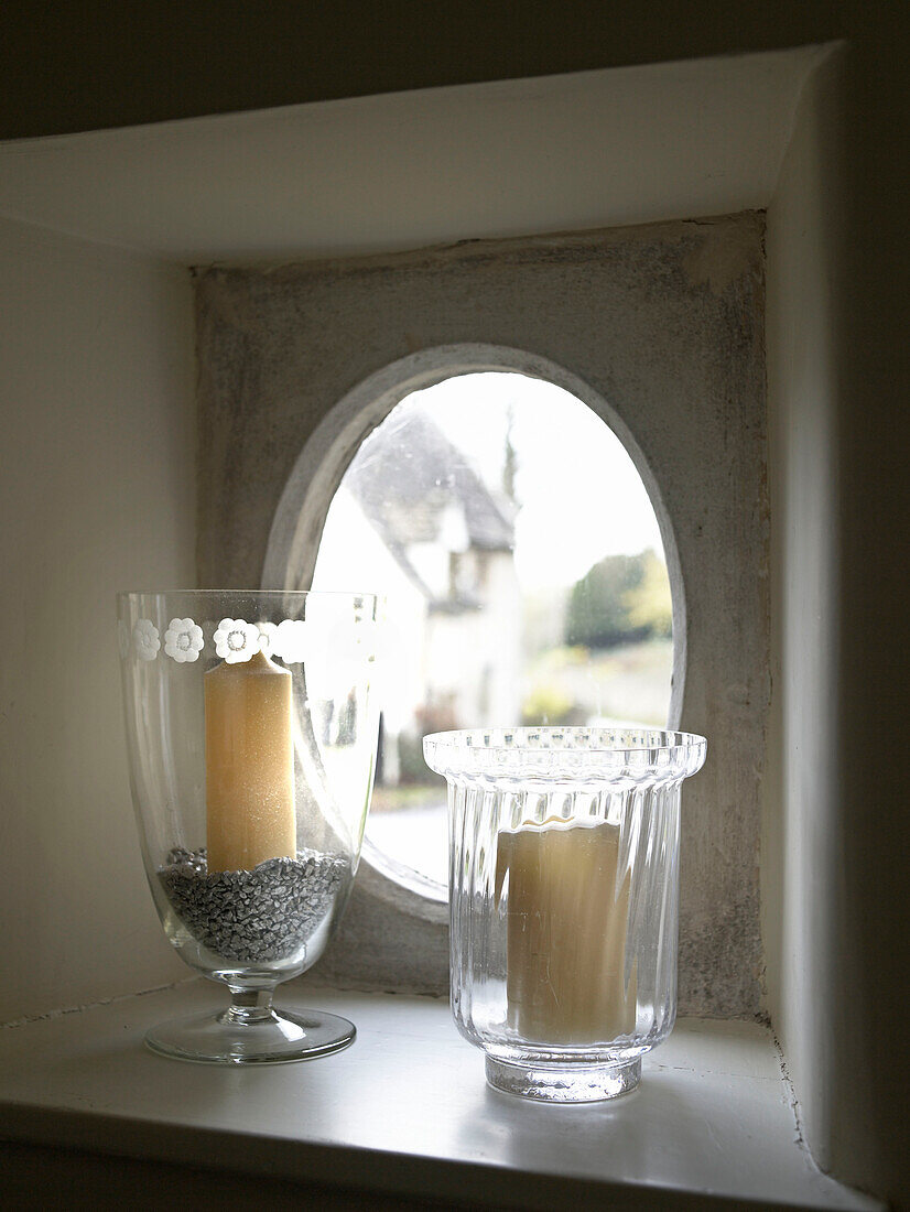 Kerzenhalter aus Glas am ovalen Fenster eines Bauernhauses in Gloucestershire, England, UK