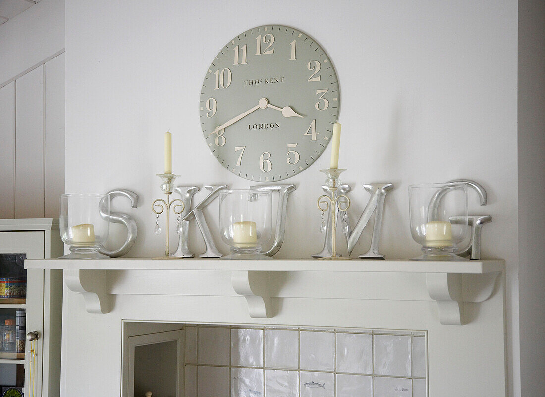 Capital letters and candles with clock on mantlepiece in kitchen of Hampshire farmhouse, England, UK