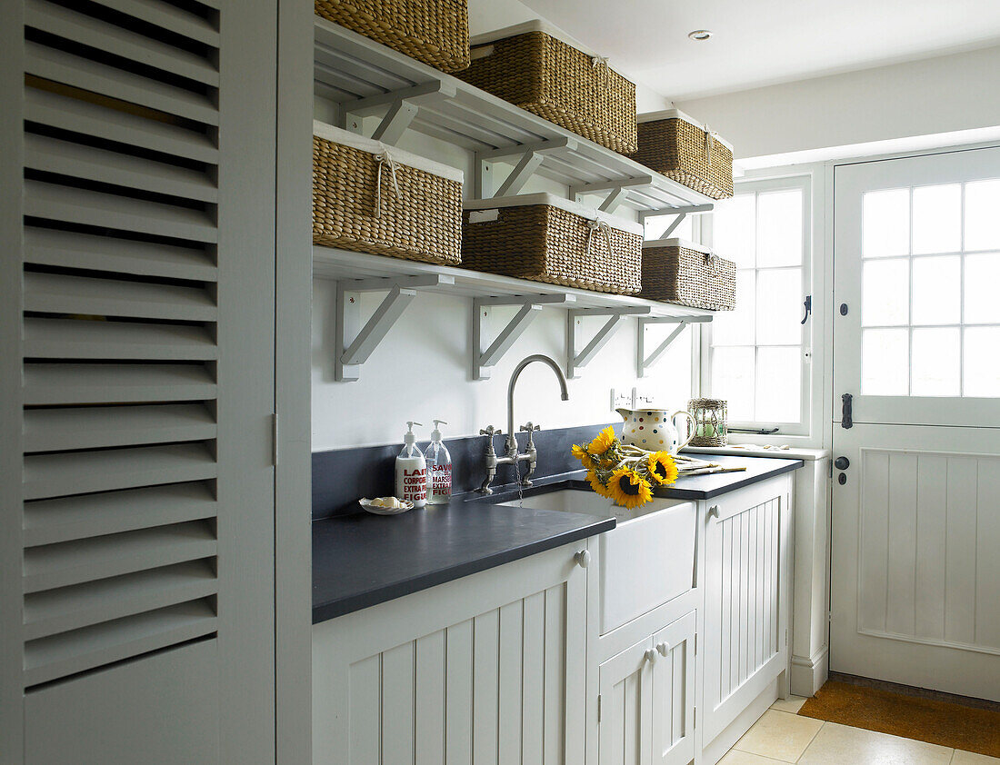 Storage baskets on open shelving above kitchen sink with cut sunflowers in Hampshire farmhouse, England, UK