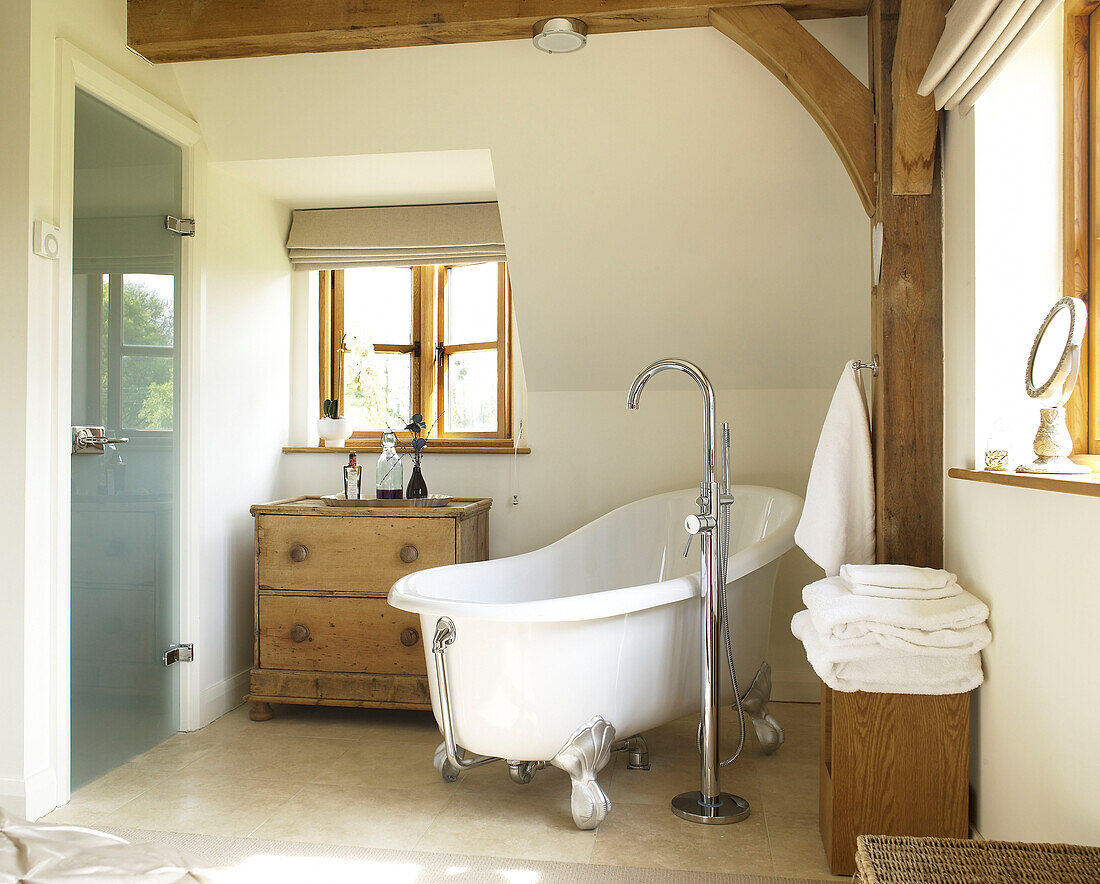Freistehende Badewanne und Milchglastür mit Holzablage im Badezimmer eines Landhauses in Gloucestershire, England