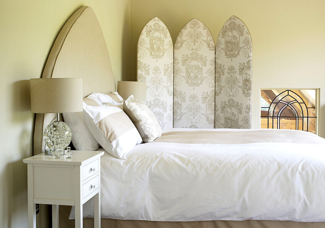 Bed with pointed arch headboard and co-ordinating cushions and folding screen Somerset new build rural England UK