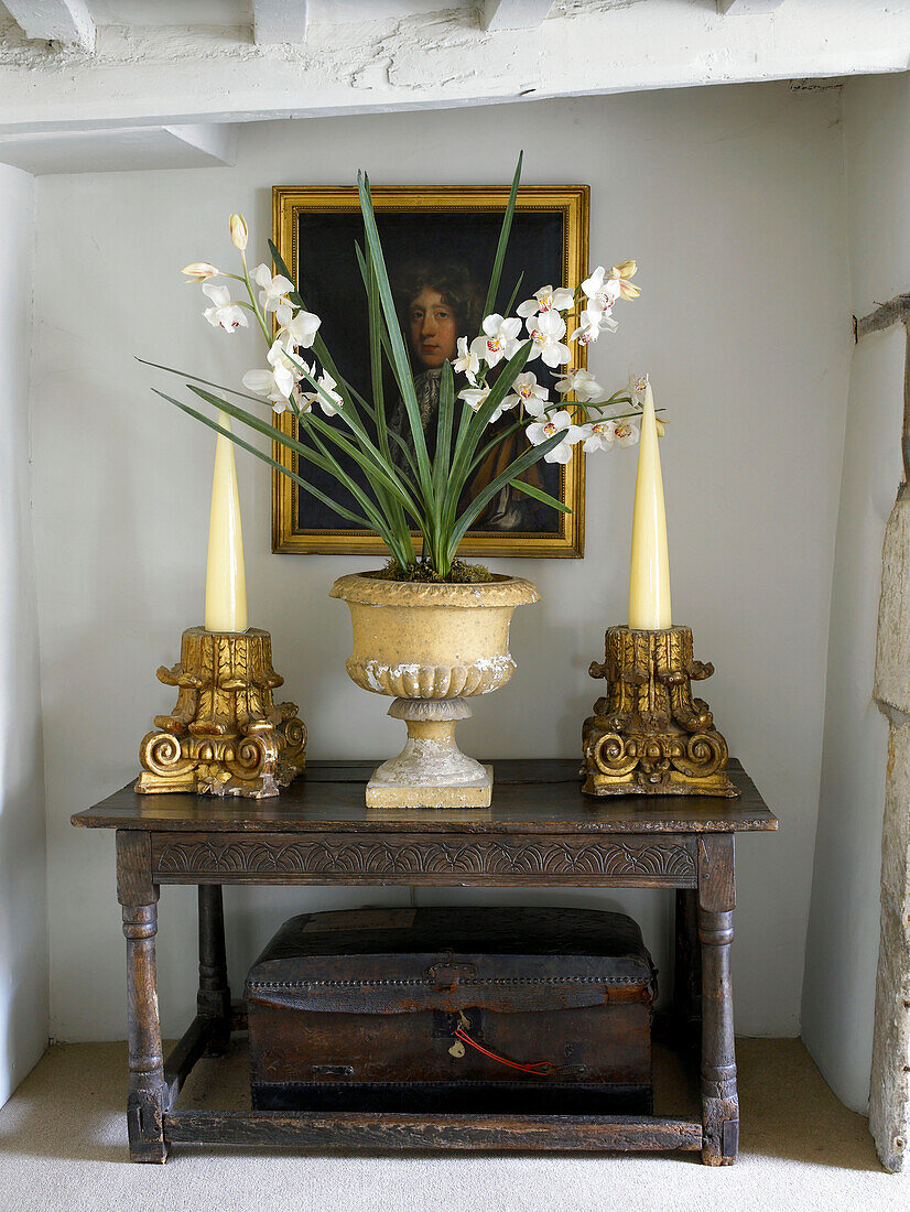 Orchidee und vergoldete Kerzenhalter auf antikem Tisch und Ölgemälde in einem Haus in Gloucestershire, England, UK
