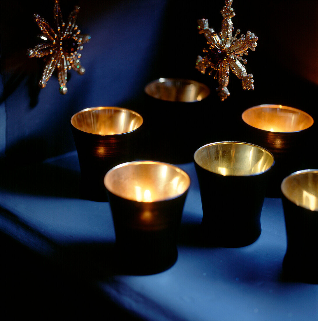 Golden leuchtende Teelichtkerzen in schwarzen Haltern, die auf einem Regal glitzern