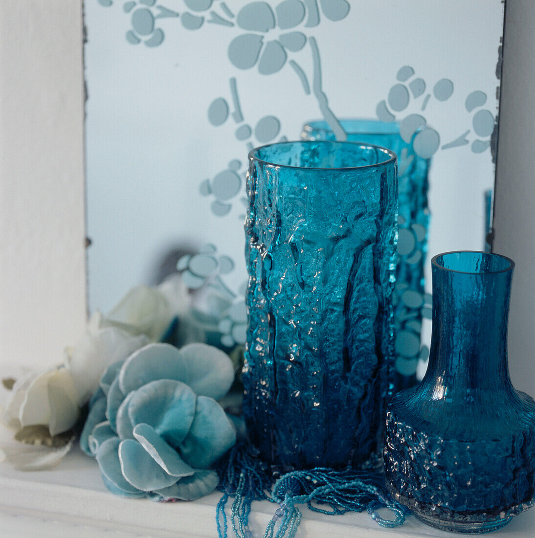 Detail von türkisblauen Glasvasen und Haushaltswaren auf einem Regal mit einem geätzten Spiegel an der Wand
