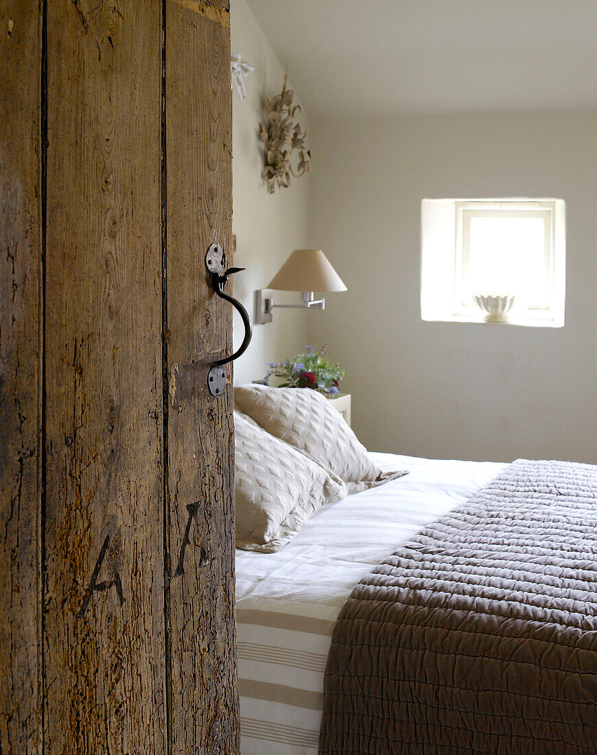 View through weathered wood door to bedroom in Gloucestershire home, England, UK