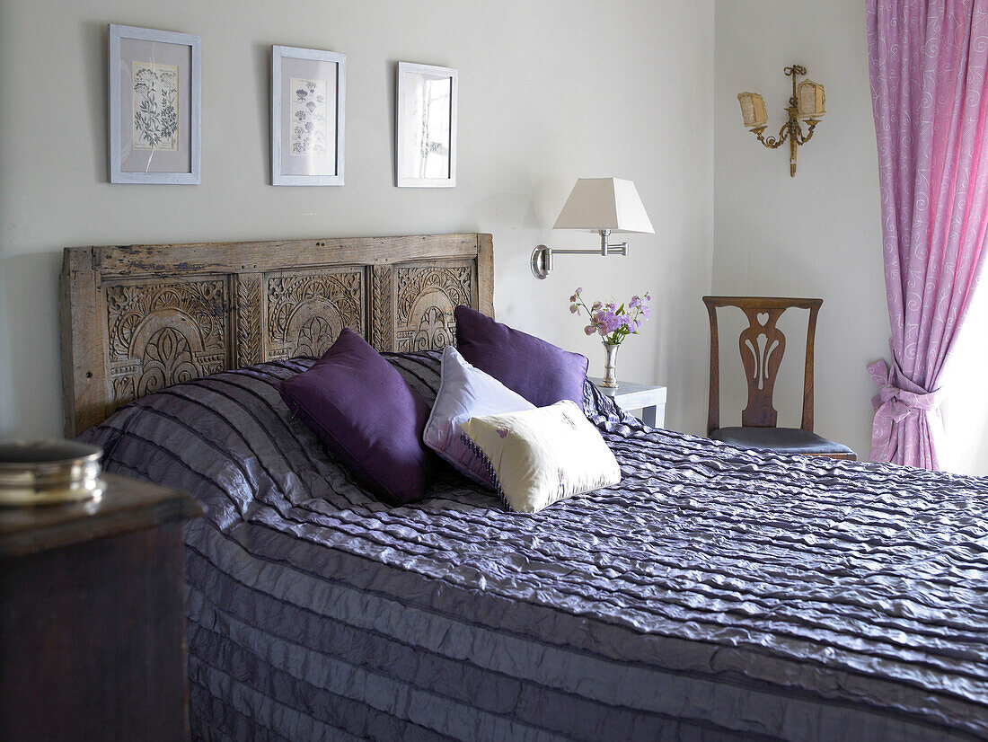 Bed in shades of purple with carved wooden headboard in Gloucestershire home, England, UK