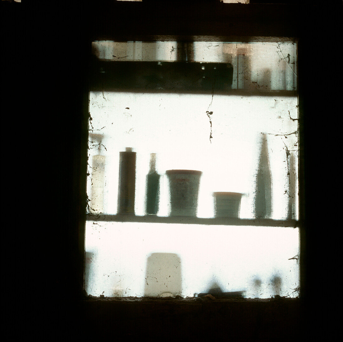 Blick aus dem Fenster eines Schuppens mit Schatten von Farbtöpfen und Heimwerkerprodukten auf Regalen
