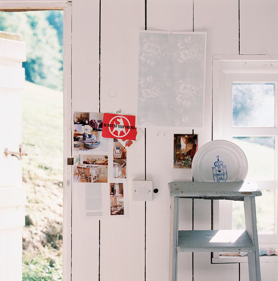 Weiß getäfelte Holzwand in einer Gartenwerkstatt mit Postkarten an der Wand und bemalte, alte Leiter