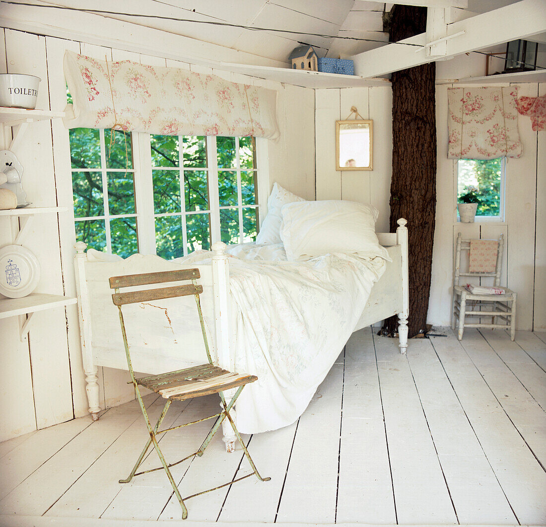 Weiß getäfeltes Baumhaus mit Bett und Stuhl
