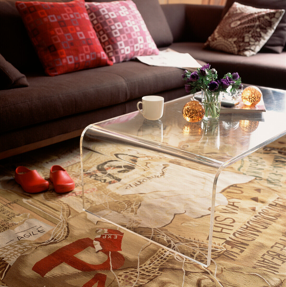 Modernes Wohnzimmer mit braunem Sofa mit Kissen, Couchtisch aus Plexiglas und gemustertem Teppich